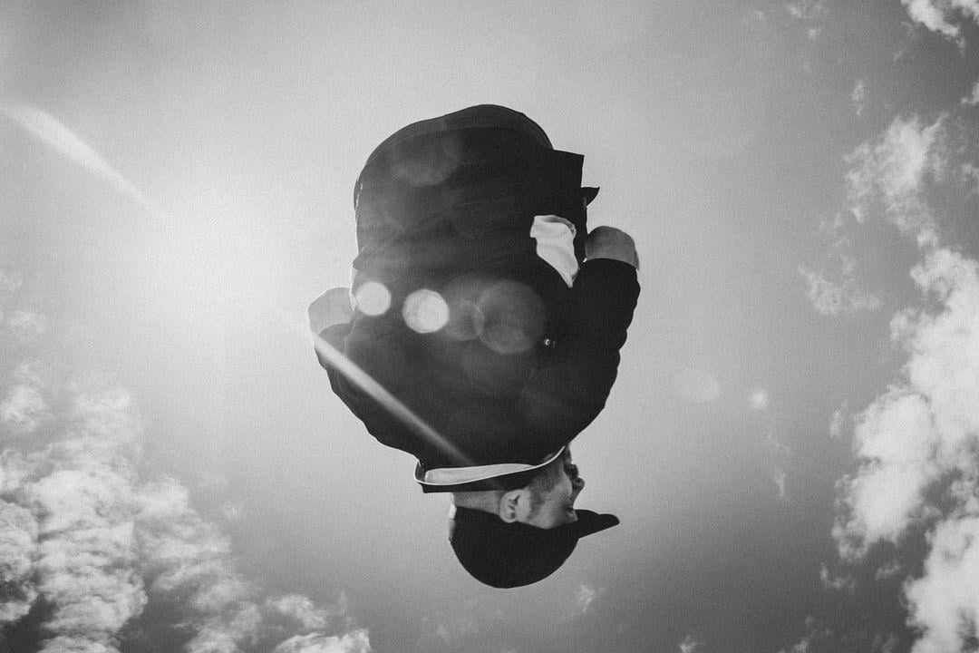 Silhouette of a person mid-air against a sunny, cloudy sky, with lens flare effect.