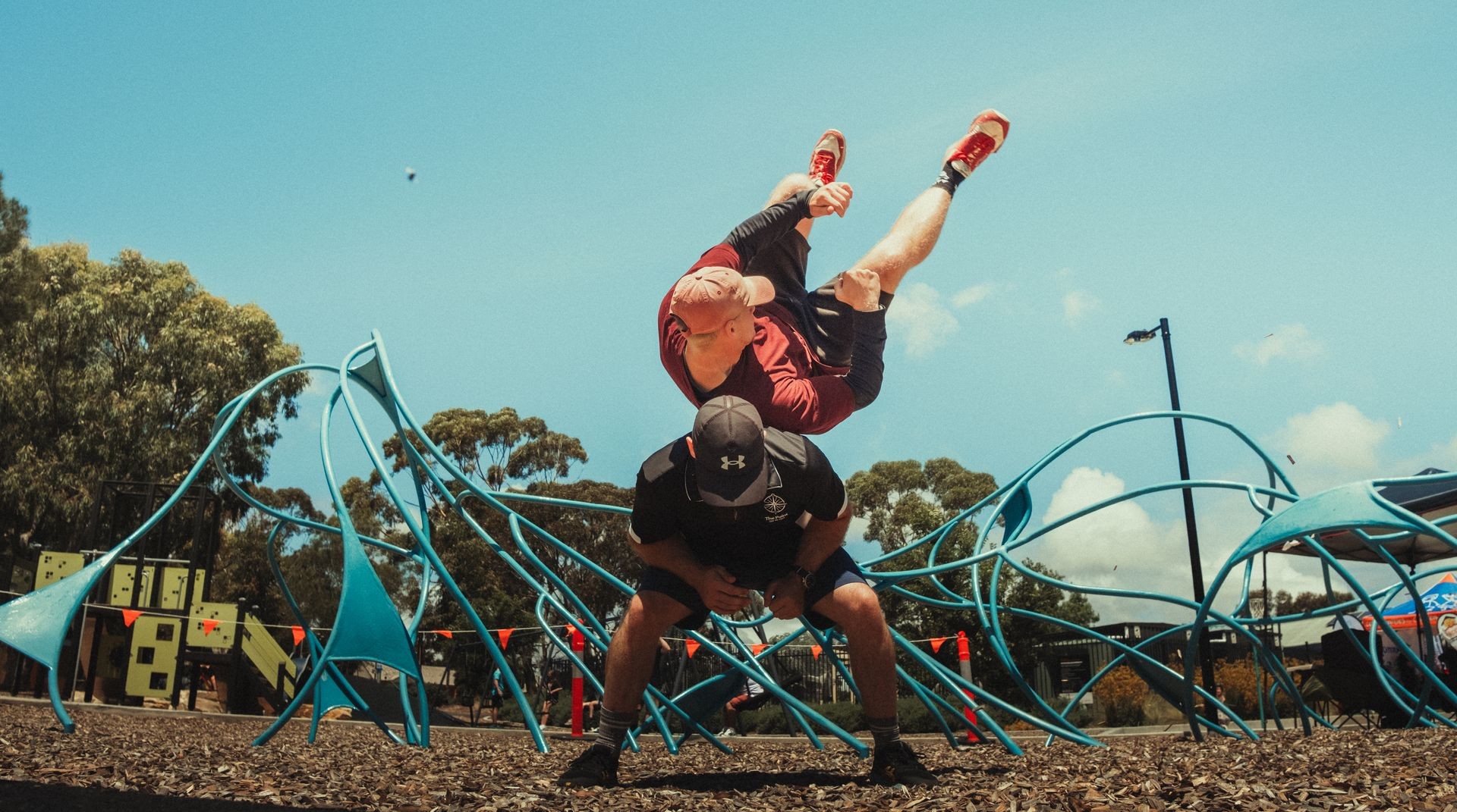 Two men performing a martial arts throw in an outdoor park with blue playground equipment in the background.